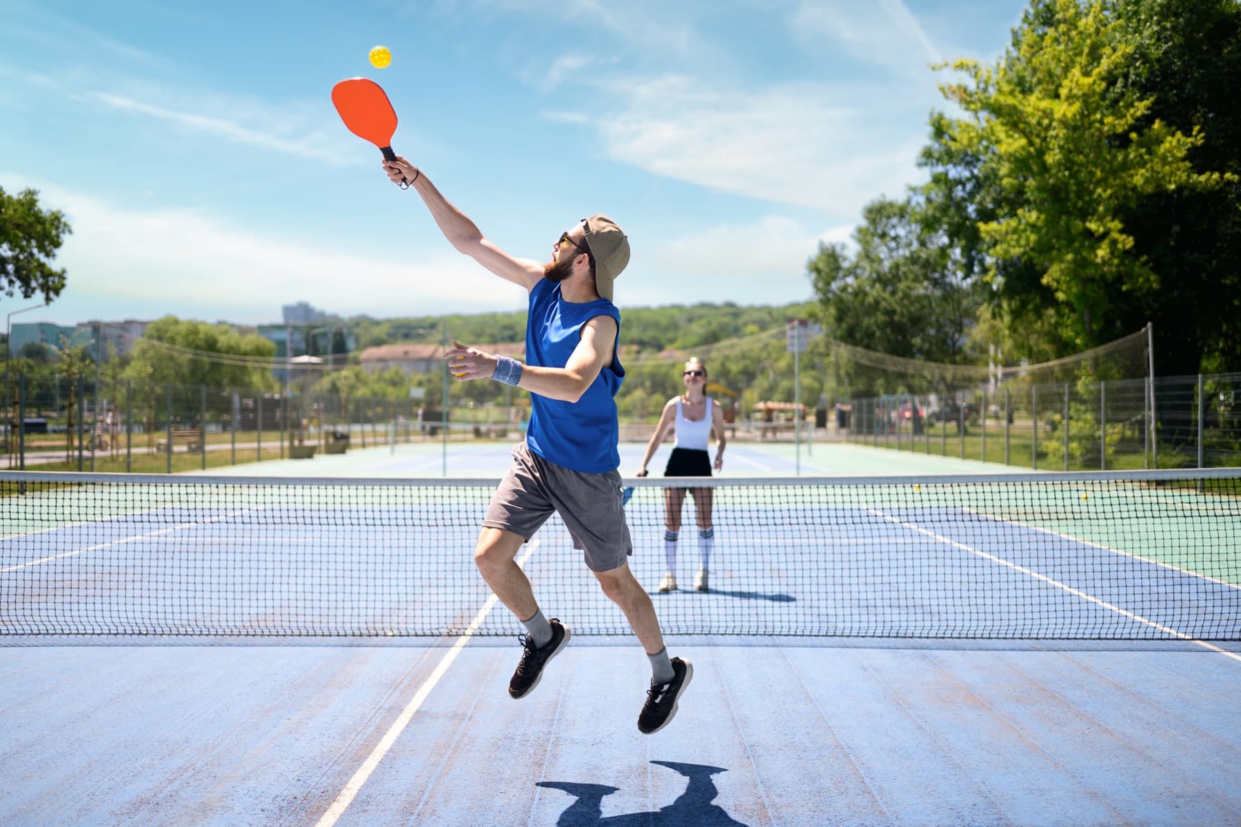 A pickleball player leaping for an overhead smash at the net